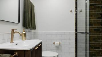 A modern bathroom with a white sink, gold fixtures, a toilet, and a glass shower enclosure.