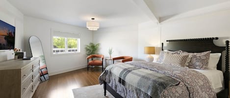 A bedroom with a large bed, a nightstand, a chair, a desk, and a window.
