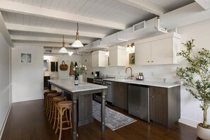 A modern kitchen with a central island, bar stools, stainless steel appliances, and pendant lighting.
