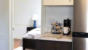 Una kitchenette compacta con cafetera, una taza y un soporte para cápsulas de café en la encimera.