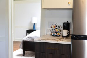 A compact kitchenette with a coffee maker, a mug, and a coffee pod holder on the counter.