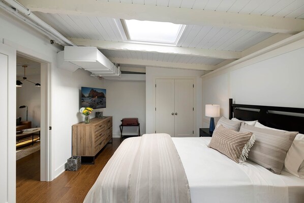 A bedroom with a bed, bedside tables, a dresser, a painting, and a skylight.