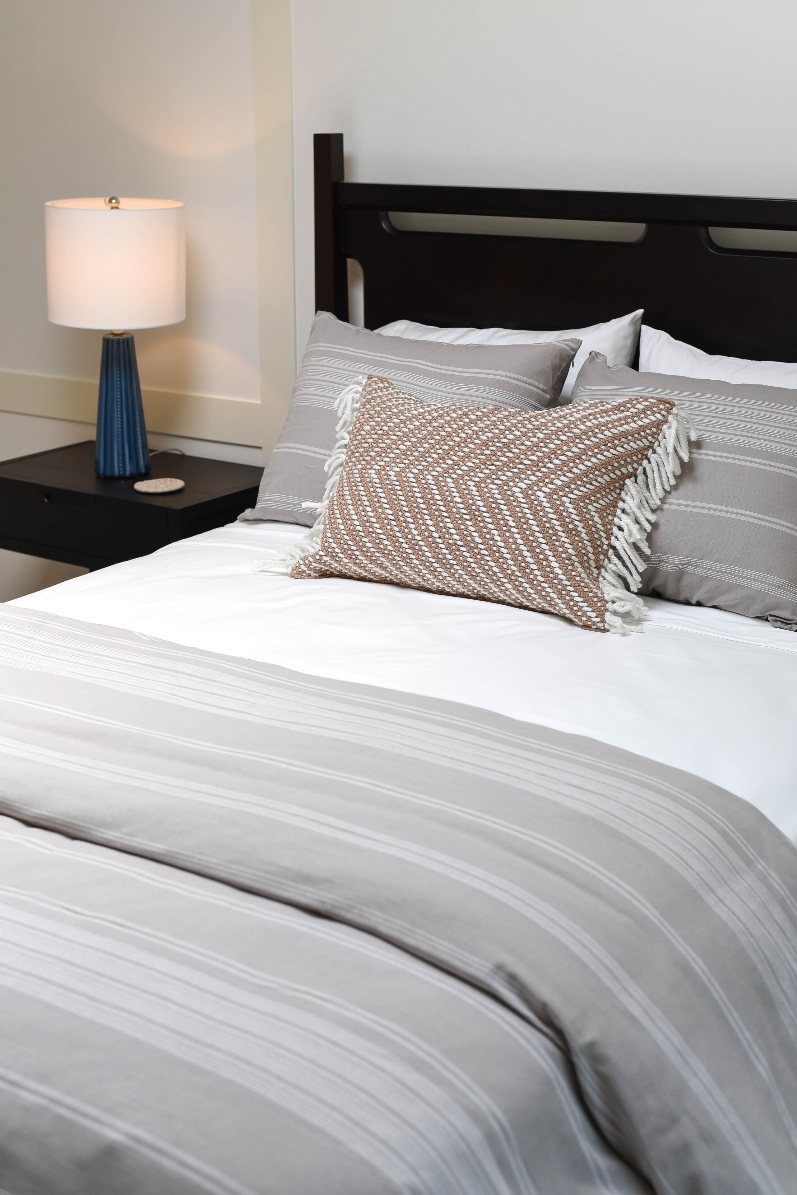 A neatly made bed with a striped bedspread, a woven throw pillow, and several pillows with striped and solid patterns.