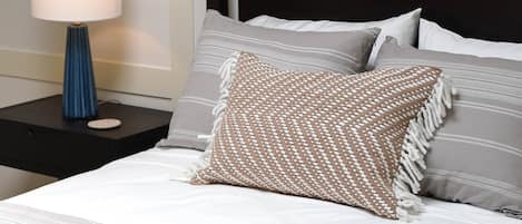 A neatly made bed with a striped bedspread, a woven throw pillow, and several pillows with striped and solid patterns.