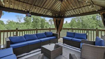 An outdoor patio with wicker furniture, a covered area, and a view of trees.