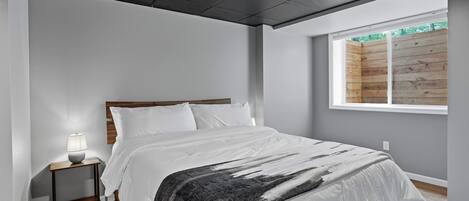 Un dormitorio con cama, mesita de noche, lámpara y ventana con vista a una valla de madera.