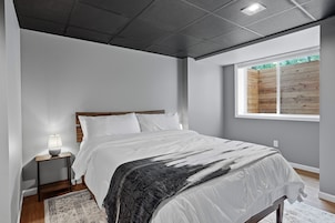Un dormitorio con cama, mesita de noche, lámpara y ventana con vista a una valla de madera.