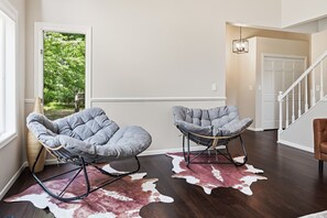 Une pièce avec deux fauteuils à bascule, un tapis en peau de vache et une vue sur la verdure par une porte.