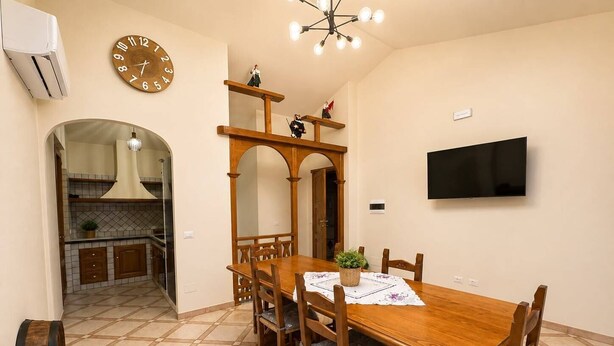 A dining area with a wooden table and chairs, a wall-mounted clock, and a television. - Sunset in Seu, 150 meters from the beach. Ideal for families and couples. (Funtana Meiga)