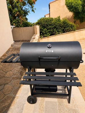 A black barbecue grill with a control panel, placed on a stone patio with a metal grill stand.