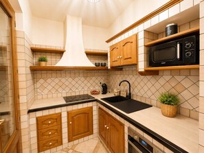 Eine kompakte Küche mit Holzschränken, einer schwarzen Arbeitsplatte, einer Mikrowelle und einem eingebauten Backofen.