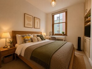 A neatly arranged bedroom with a bed, bedside lamps, a desk, and a television. - Stylish 2-BRs Flat with AC near Oxford Street (London)