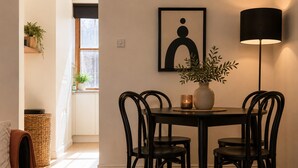 Ein Essbereich mit rundem Tisch, vier Stühlen, einer Pflanzvase, einem gerahmten Kunstwerk und einer Stehlampe.