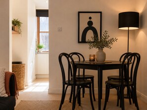 A dining area with a round table, four chairs, a vase with plants, a framed artwork, and a floor lamp. - Stylish 2-BRs Flat with AC near Oxford Street (London)