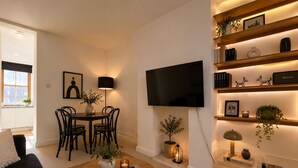 Ein modernes Wohnzimmer mit Sofa, Couchtisch, Fernseher und einem Essbereich mit Stühlen und Tisch.
