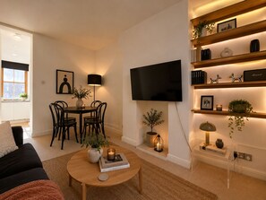 A modern living room with a sofa, coffee table, TV, and a dining area with chairs and a table. - Stylish 2-BRs Flat with AC near Oxford Street (London)