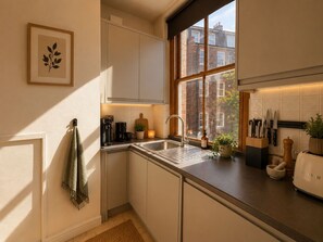 Eine moderne Küche mit integriertem Spülbecken, einer Kaffeemaschine, einem Toaster und einem Fenster mit Blick auf ein Backsteingebäude.