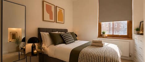 A bedroom with a bed, bedside table, lamp, and artwork.