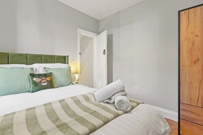 Ein Hotelzimmer mit einem Bett, einem grünen gepolsterten Kopfteil, einer gestreiften Decke und einem Holzschrank.
