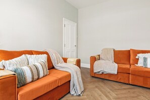 Ein Zimmer mit zwei orangenen Sofas, einer weißen Tür und einem Holzboden.