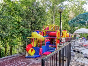 Ein Spielplatz mit Rutschen und Klettergerüsten, umgeben von Bäumen.