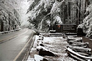 A road leading to Great Smoky Mountains National Park with a signboard and snow-covered trees. - Brand NEW Luxury 3/3.5 Cabin! AMAZING VIEW! Indoor Pool, Huge Game Room, WIFI. (Gatlinburg)