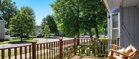 Une terrasse en bois avec une chaise suspendue, une balustrade et une vue sur une rue résidentielle.