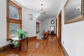 Ein Flur mit Holzboden, einem Chandelier und einem großen Spiegel an der Wand.