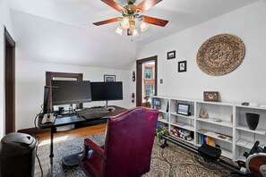 Ein Arbeitszimmer mit Schreibtisch, zwei Monitoren, einem Stuhl, einem Laufband und einem Deckenventilator.