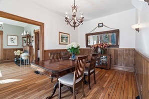 A dining room with a wooden table and chairs, a chandelier, and a mirror on the wall. - The Blue Victorian | Near Downtown Traverse City (Traverse City)
