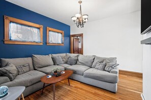 A living room with a sectional sofa, a wooden coffee table, and a chandelier. - The Blue Victorian | Near Downtown Traverse City (Traverse City)