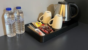 A tray with two water bottles, two white mugs, a silver electric kettle, and a variety of packaged snacks.