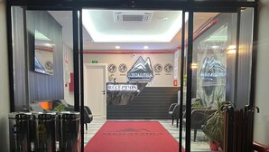 A hotel reception area with a red carpet leading to a reception desk, a staircase, and a wall-mounted sign.