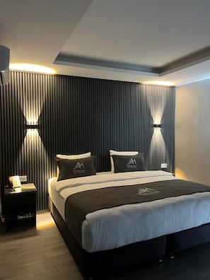 Una habitación de hotel moderna con una cama grande, dos mesitas de noche y una lámpara fijada a la pared.