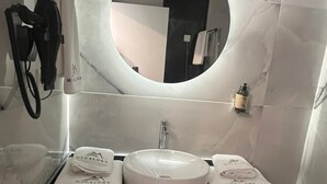 A bathroom with a round mirror, two sinks, and towels with a logo.