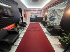 Un espace d’accueil avec un tapis rouge, des fauteuils en cuir noir, un comptoir de réception et un mur en marbre.