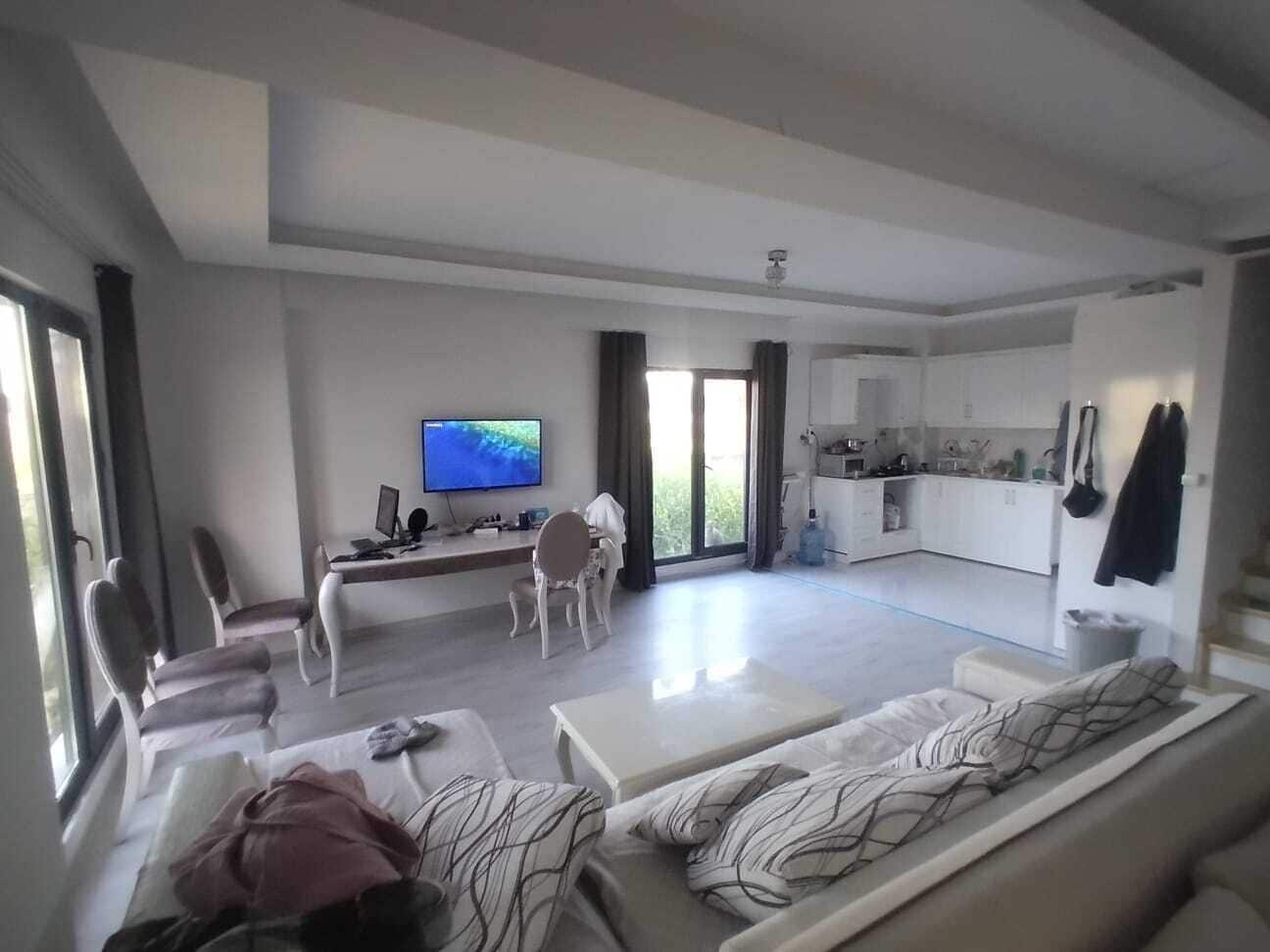A modern living room with a sofa, a TV, and a dining area with a table and chairs.
