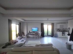 Amplia sala de estar con sofá, mesa de comedor, sillas, televisor y cocina al fondo.