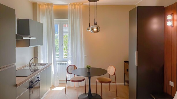 A modern kitchen with a dining area, a large window with curtains, and a ceiling light fixture. - Flatsharing Design Studio - Moka (Milan)