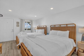 Ein Hotelzimmer mit zwei Betten, einem hölzernen Kopfteil, einem Nachttisch mit Lampe, einem Fenster mit Vorhängen und einer Tür.