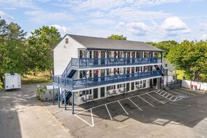 Ein zweigeschossiges Gebäude mit Balkon, Parkplatz und einem kleinen Anbau.