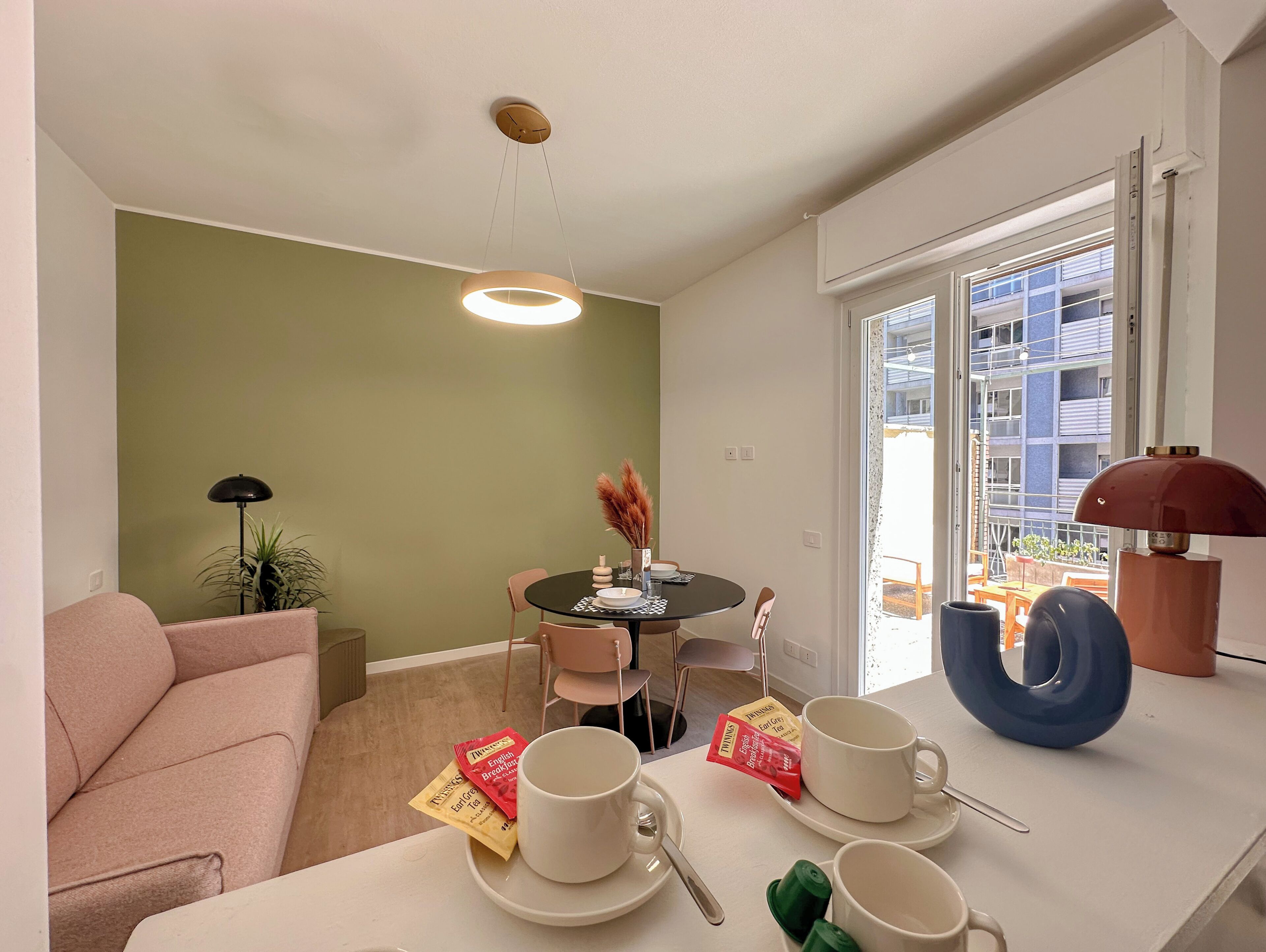 Een moderne woonkamer met een bank, een eettafel met stoelen, een bijzettafeltje en een raam met uitzicht op een gebouw.