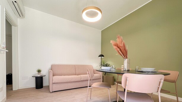 Ein zeitgemäßer Wohnbereich mit Sofa, Esstisch, Stühlen und einem kleinen Beistelltisch mit Pflanze.