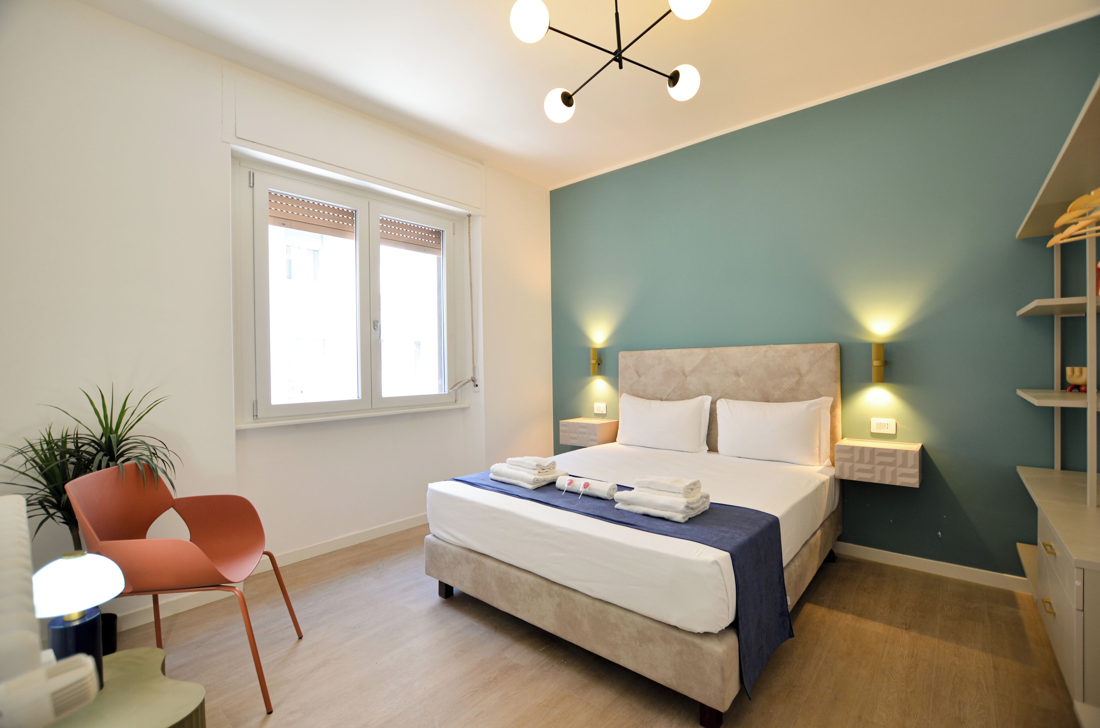 Una camera d'albergo con un letto, comodini, una sedia, una finestra e una pianta.