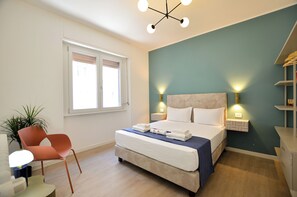 Une chambre d’hôtel avec un lit, des tables de chevet, une chaise, une fenêtre et une plante.