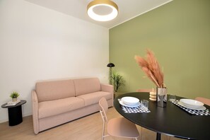 A modern living room with a sofa, a dining table with chairs, a lamp, and a plant. - Flatsharing - Campanini City Terrace (Milan)