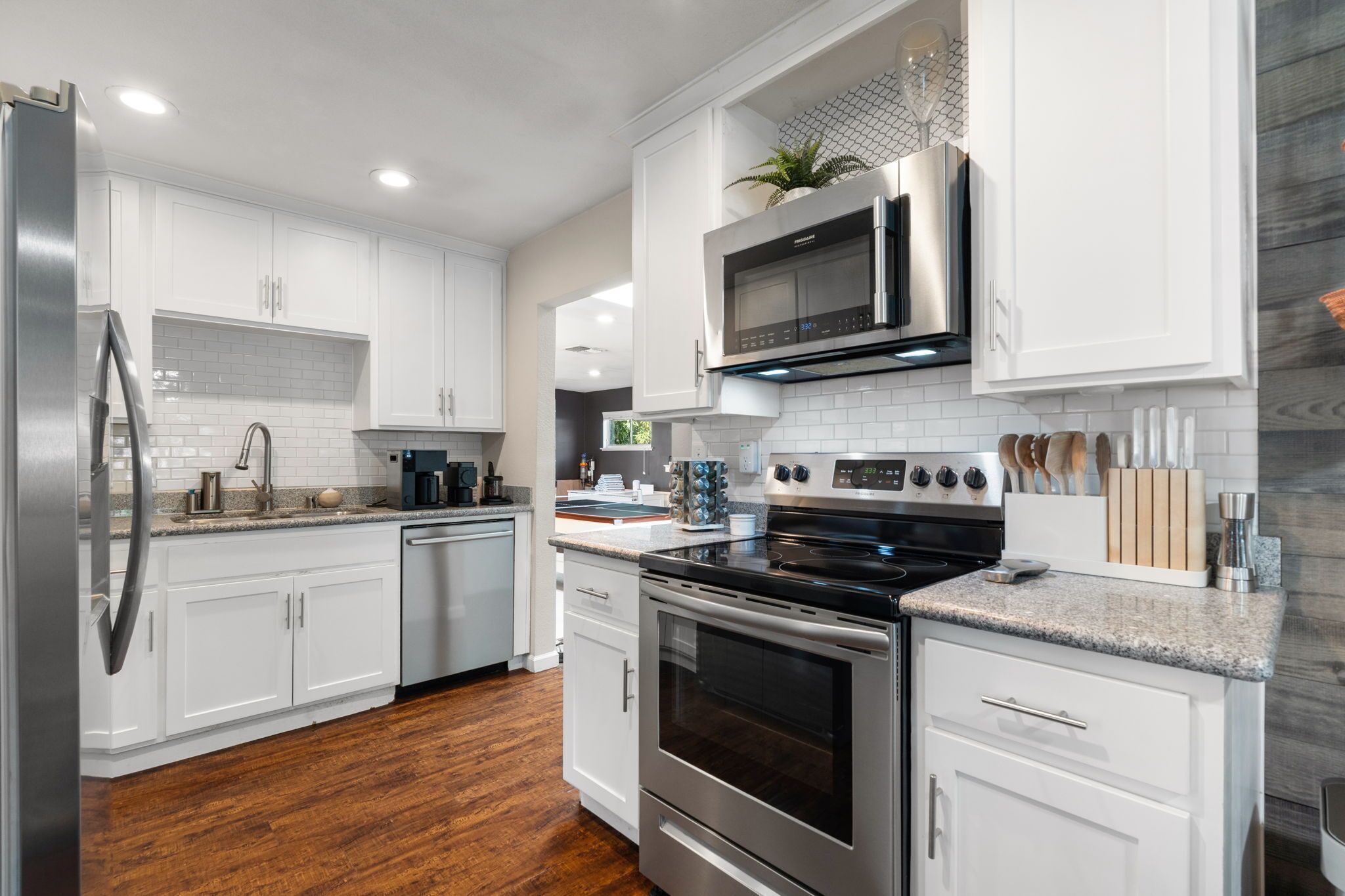 Una cocina moderna con armarios blancos, electrodomésticos de acero inoxidable y piso de madera.