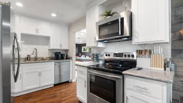 Una cocina moderna con armarios blancos, electrodomésticos de acero inoxidable y piso de madera.