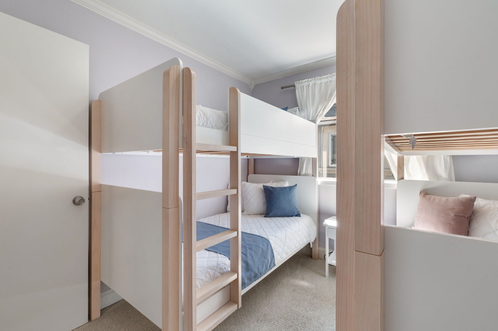 A room with bunk beds, a desk, and a window with curtains.