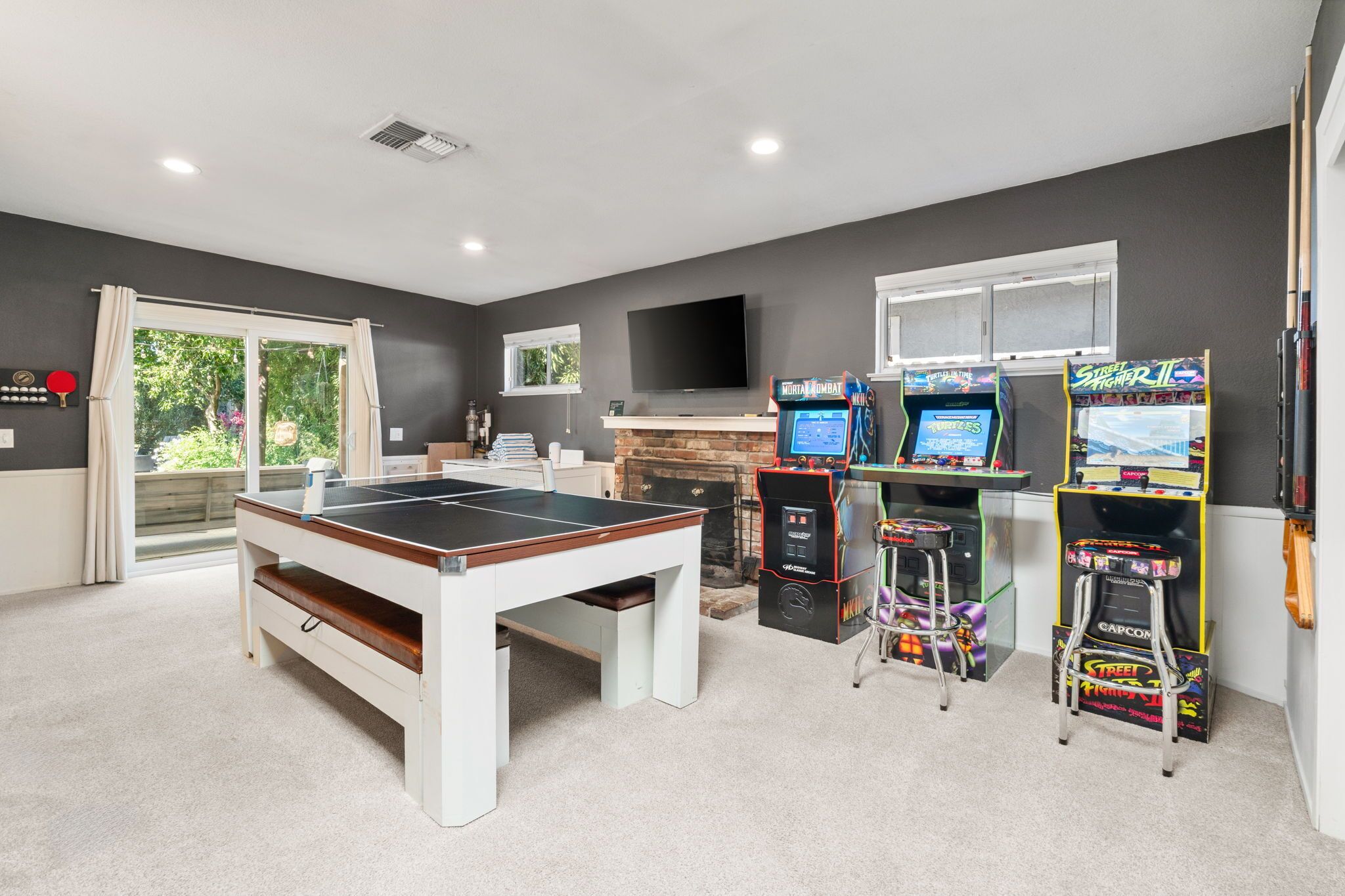A room with a ping pong table, arcade games, a TV, and a fireplace.